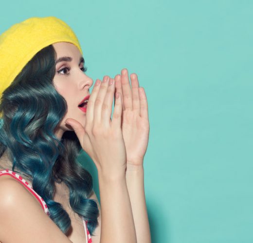 Beautiful woman in a yellow beret makes speaker from her hands. On a blue background.